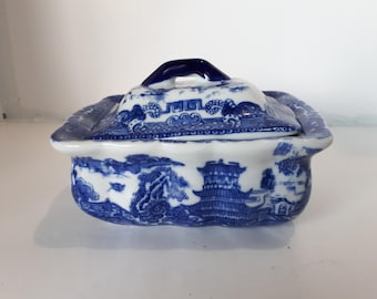 May include: A blue and white ceramic trinket box with a lid. The box and lid feature a detailed Willow pattern design. The lid has a small handle. The box is a rectangular shape with scalloped edges.