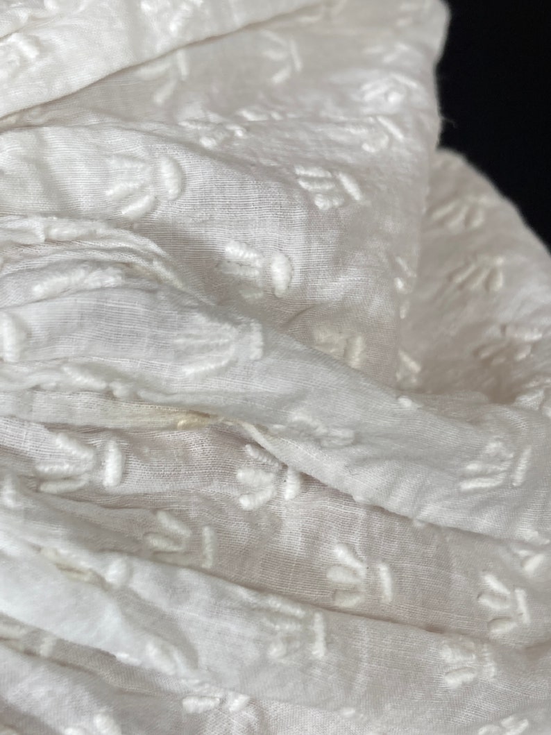 May include: White fabric with a delicate embroidered pattern. The fabric is soft and sheer, with a subtle texture.