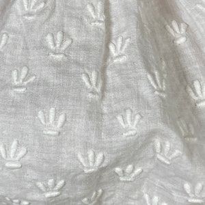 May include: White fabric with a repeating pattern of embroidered flower shapes.