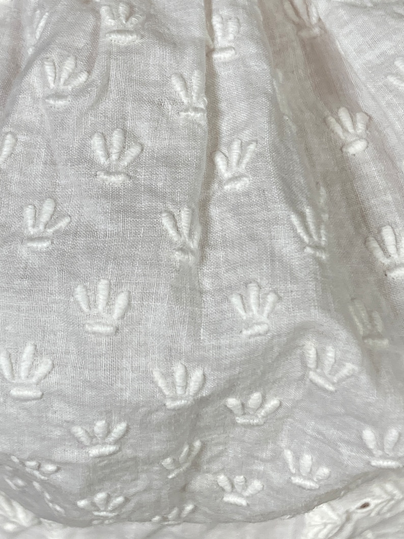May include: White fabric with a repeating pattern of embroidered flower shapes.