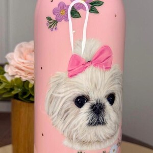 Op de afbeelding: Roze waterfles met een illustratie van een witte hond met een roze strik. De fles heeft het woord "owala" op het deksel en de naam "Agnes" op de bodem. Bloemen- en hartaccenten versieren de fles.