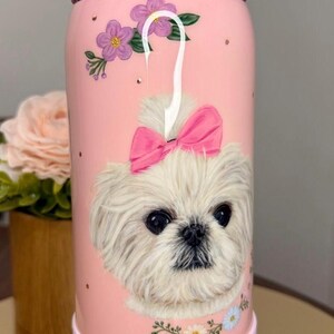 Op de afbeelding: Roze ge&iuml;soleerde waterfles met een illustratie van een witte hond met een roze strik. De fles heeft een roze deksel en basis, met de merknaam "owala" erop gedrukt. Bloemen- en stipaccenten versieren de fles.