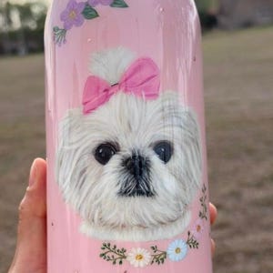 Op de afbeelding: Roze Owala waterfles met een illustratie van een witte hond, een roze strik, bloemmotieven en de naam "Agnes". De fles heeft een roze deksel en een inhoud van ongeveer 710 ml.