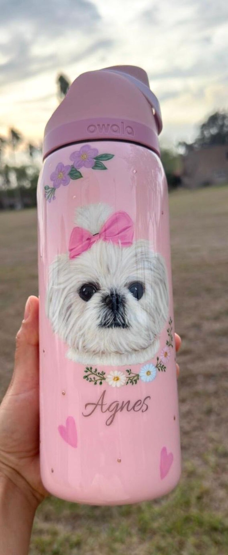 Op de afbeelding: Roze Owala waterfles met een illustratie van een witte hond, een roze strik, bloemmotieven en de naam "Agnes". De fles heeft een roze deksel en een inhoud van ongeveer 710 ml.