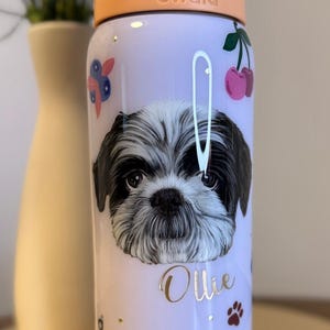 Op de afbeelding: Een lichtpaarse Owala waterfles met een zwart-wit portret van een Shih Tzu hond en de naam "Ollie" in gouden letters. De fles is versierd met kersen en pootafdrukken.