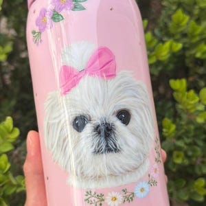 Op de afbeelding: Roze Owala waterfles met een illustratie van een witte hond met een roze strik, bloemen en de naam "Agnes". De fles heeft een roze deksel en handvat en is versierd met kleine gouden stippen.