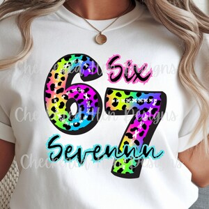 May include: White t-shirt with a colorful graphic design. The design features the numbers "67" in a leopard print pattern, with the words "Six" and "Seventeen" in a playful font. The shirt is a casual style.