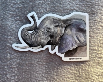 May include: A watercolor illustration of an elephant's head with its trunk raised. The elephant is painted in shades of gray and purple, with a white background. The image is signed with the artist's Instagram handle, @raedianeart.