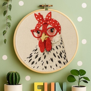 May include: A circular wooden embroidery hoop containing a fabric panel with a stitched illustration of a white chicken with black speckles. The chicken wears red-rimmed glasses and a red headscarf with white polka dots on its head.