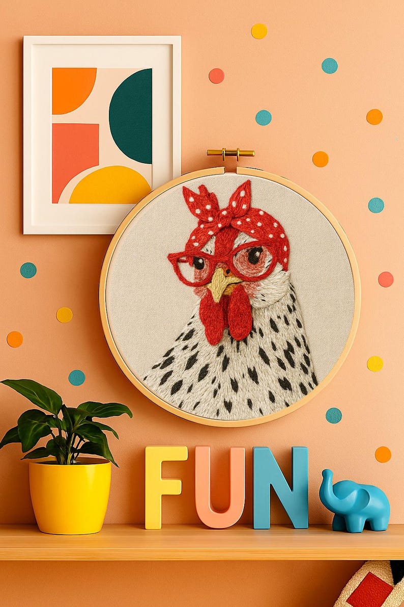 May include: A circular embroidery hoop featuring a stitched image of a white chicken with black spots, wearing red glasses and a red polka-dot headscarf. The chicken has a yellow beak and red wattle, set against a light beige fabric background.