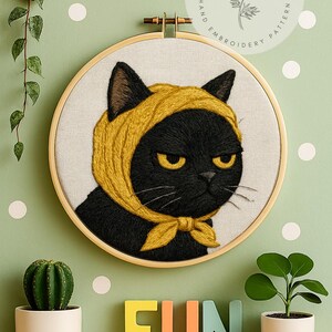 以下が含まれることがあります： 黄色いスカーフとリボンをつけた黒猫の刺繍アート。猫は黄色い目をし、不機嫌そうな表情をしています。背景は、白い水玉模様の薄緑色の壁です。「FUN」という言葉がカラフルな文字で表示されています。