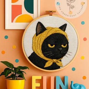以下が含まれることがあります： 黄色いスカーフをつけた黒猫の刺繍。不機嫌そうな表情と黄色の目。刺繍枠の下にはカラフルな文字で「FUN」と書かれています。抽象的なポスターと鉢植えの植物も表示されています。