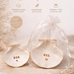 Puede incluir: Dos recuerdos de bautizo blancos en forma de concha con ribete dorado, personalizados con los nombres "ZOE" y "BEL". La imagen incluye texto: "Recuerdos de bautizo, Pequeños regalos, grandes recuerdos."