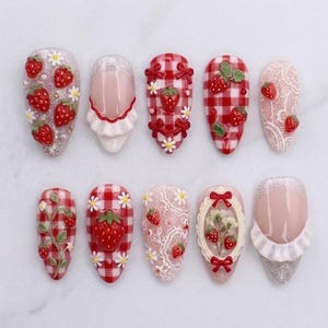 May include: A set of ten press-on nails featuring various designs including red and white gingham patterns, white lace textures, silver glitter accents, 3D strawberry charms, small white daisy embellishments, red bows, and white ruffled edges.