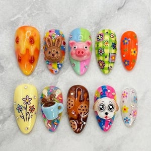 May include: A collection of ten artificial nails with various designs. The designs include a bunny, pig, flowers, and a dog. The nails feature bright colors like orange, yellow, blue, and pink, with some nails having 3D elements.