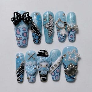 Peut inclure: Un ensemble de dix faux ongles avec une base bleu clair, des motifs léopard roses, des rayures zébrées noires et blanches, et des paillettes. Les décorations incluent un gros nœud noir à pois, des clous argentés, des perles et une figurine Hello Kitty.