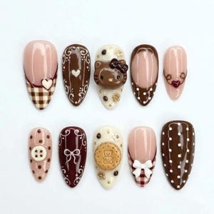 May include: A set of ten press-on nails featuring brown, cream, and white designs. Patterns include brown gingham, white polka dots, intricate swirls, and 3D embellishments like a brown cat face, a teddy bear cookie, a white button, and bows.