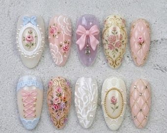 May include: A collection of ten artificial nails with various designs. The nails feature intricate details, including floral patterns, bows, lace, and pearl accents. Colors include pink, white, gold, and lavender, creating an elegant and feminine aesthetic.