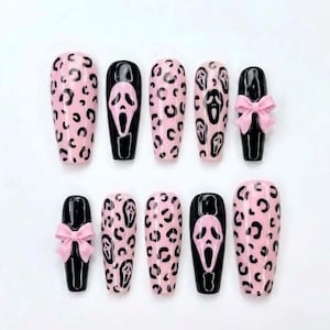Peut inclure: Un ensemble de dix faux ongles avec des motifs variés. Certains ongles présentent une base rose clair avec des taches de léopard noires, tandis que d'autres sont noirs unis avec un motif de masque de fantôme blanc ou un nœud rose en relief.