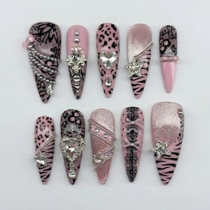 May include: A set of ten almond-shaped press-on nails featuring a pink, black, and silver color palette. The designs include black lace patterns, pink leopard and zebra prints, silver glitter, rhinestones, heart-shaped crystals, and star charms.