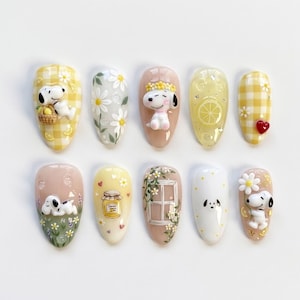 May include: A set of ten press-on nails featuring Snoopy character designs, yellow gingham patterns, white daisies, a lemon slice, a small red heart, a jar of honey, a window frame, and floral accents in a variety of soft pastel colours.