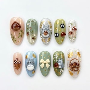 May include: A set of ten press-on nails featuring various designs including a 3D chestnut, hand-painted vines with white flowers, a 3D gray Totoro character, soot sprites, mushrooms, a plaid acorn, a cream-colored bow, and a basket of acorns.