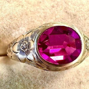 May include: A silver ring with an oval-shaped, faceted, pink gemstone set in a floral design.