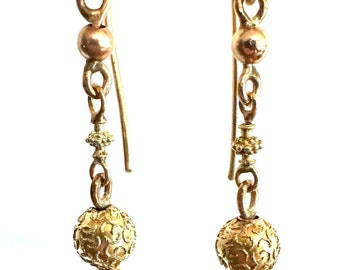May include: A pair of gold dangle earrings with a textured ball charm and a smaller gold bead. The earrings have a simple hook closure.