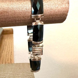 May include: A black onyx bracelet with silver accents. The bracelet is made of faceted onyx stones and silver links. The clasp is a silver box clasp with a small silver pin.