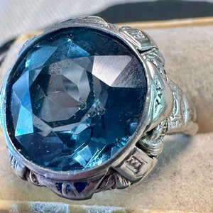 May include: A silver ring with a large, faceted, blue gemstone set in a decorative, ornate setting.