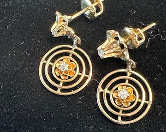May include: A pair of gold dangle earrings with a circular design and a small diamond in the center of each flower.