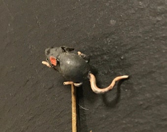 May include: A gold pin with a black mouse figurine on top. The mouse has red eyes and a curled tail.