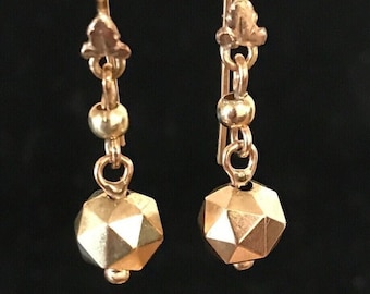 May include: A pair of gold dangle earrings with a faceted geometric bead and a small gold bead on each earring.