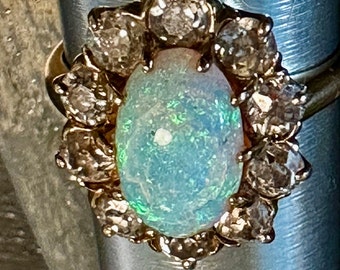 May include: A gold ring with a large oval opal surrounded by a halo of smaller diamonds.