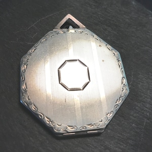 May include: Silver octagonal locket with a decorative border and a smaller octagon in the center. The locket has a hinged closure.