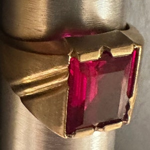Könnte beinhalten: Ein goldener Ring mit einem großen, rechteckigen, dunkelroten Edelstein.