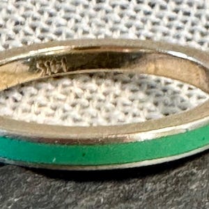 May include: A thin gold band ring with a green enamel stripe around the edge.