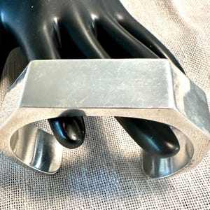 May include: A silver hexagonal bangle bracelet with a smooth, polished finish.