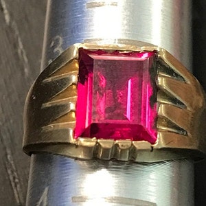 May include: A gold ring with a large, square, bright pink gemstone.