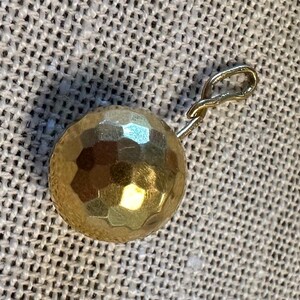 May include: A gold-toned pendant with a textured, faceted ball charm and a simple loop for attaching to a chain.