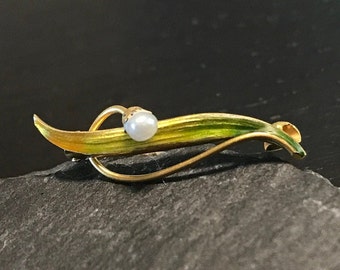 May include: A gold-toned brooch with a green and yellow enamel leaf design and a single pearl accent.