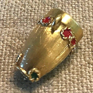 May include: A gold-colored metal pin shaped like a drum with red and green enamel accents.