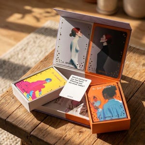 Op de afbeelding: Een kaartspel in een open doos met geïllustreerde kaarten met figuren en het woord SPACE. Eén kaart bevat de tekst: Which part(s) of you has been affecting you the most, lately? De kaarten tonen diverse artistieke scènes met kleurrijke figuren.