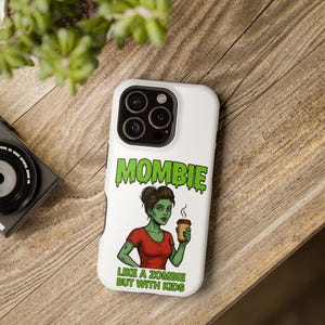 May include: White phone case featuring the word "MOMBIE" in green, with a cartoon zombie woman holding a coffee cup. The text "LIKE A ZOMBIE BUT WITH KIDS" is below the image. The case is on a wooden surface.