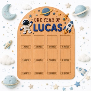 May include: A wooden milestone board with an arched top featuring the text ONE YEAR OF LUCAS. It includes twelve square photo slots labelled from 1 MONTH to 12 MONTHS. The board is decorated with 3D space-themed icons including an astronaut, a rocket, a planet with rings, and stars.