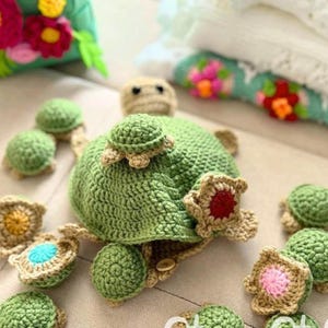 May include: A handmade green crochet turtle hat with a small turtle on top, surrounded by smaller turtle-shaped crochet pieces. The hat has tan accents and a button closure. The crochet work is detailed and the colors are vibrant.