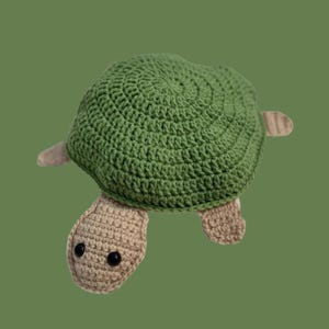 Könnte beinhalten: Handgefertigte Häkelschildkröte. Der Panzer ist grün, Kopf und Gliedmaßen sind beige. Die Augen sind schwarz. Die Schildkröte ist aus Garn gefertigt. Der Panzer hat einen Durchmesser von ca. 15 cm. Ein handgefertigter Artikel.