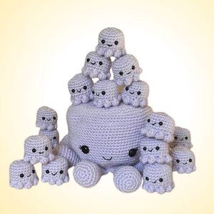 May include: A crocheted lavender octopus with a smiling face, surrounded by smaller crocheted octopus figures. The octopus has large, black eyes and is surrounded by 14 smaller octopuses. The background is a gradient of yellow and white.