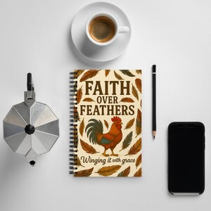 May include: A spiral-bound notebook with the text "FAITH OVER FEATHERS" and a rooster illustration. The notebook is surrounded by brown feathers. A cup of coffee, a pencil, a phone, and a coffee maker are also in the image.
