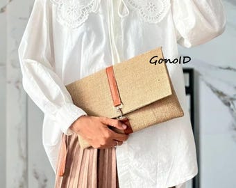 May include: A beige clutch with a brown leather strap and accents is held in front of a white blouse with a lace collar. The text "Gonold" is visible on the clutch.